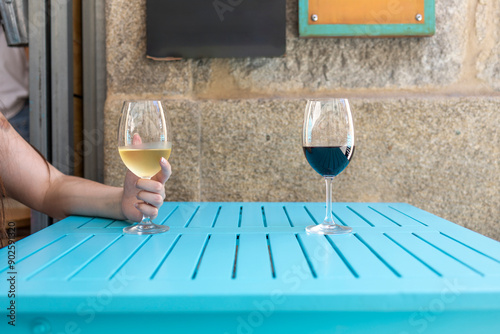 A minimalist scene featuring two wine glasses, one filled with red wine and the other with white wine, resting on a bright blue table with a rustic stone wall as the backdrop.