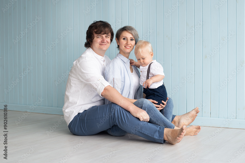 Happy parents. Mother, father and their son baby boy having good time at home near blue wall Happy parents. Mother, father and their son baby boy having good time at home near blue wall