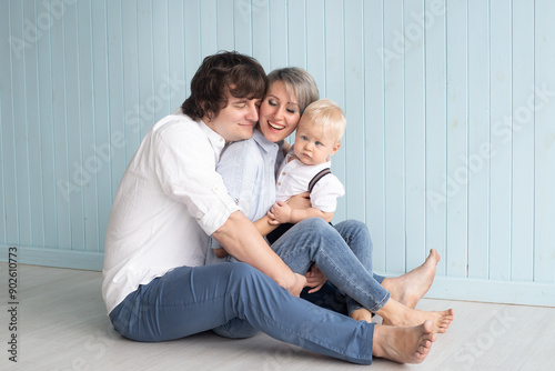 Happy family, mother, father and their son baby boy hugging at home while sitting near blue wall.