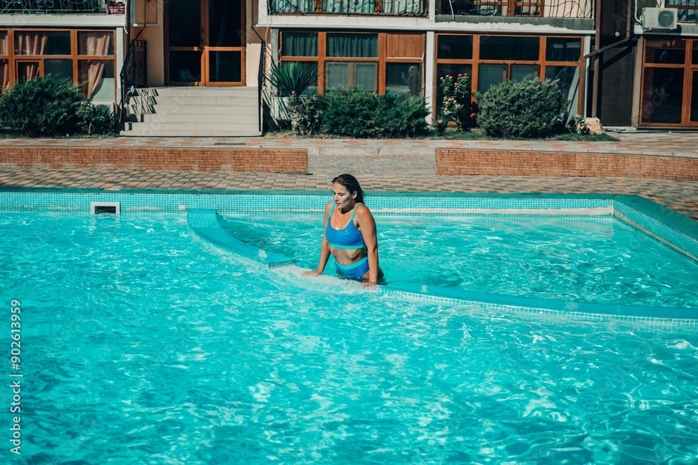 Naklejka premium A woman is in the water, smiling and enjoying herself. The water is blue and the pool is surrounded by a white ledge.