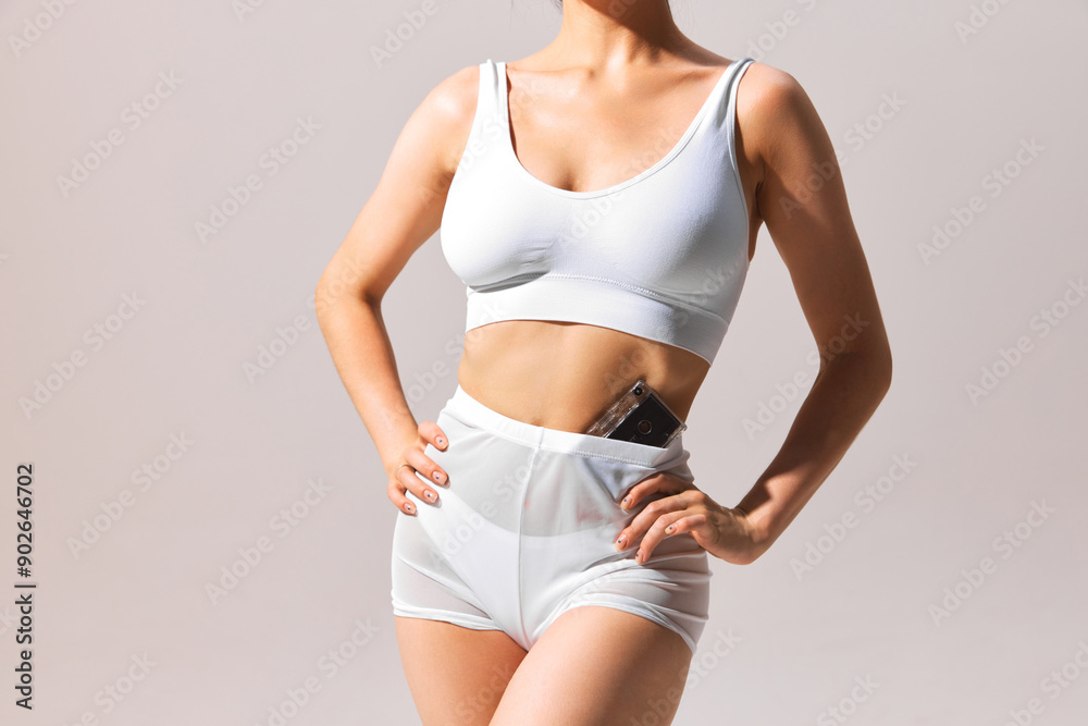 Cropped image of slim female body, model posing in underwear with vintage cassette on grey background. Concept of retro and vintage, summer vibe, body aesthetics Cropped image of slim female body, model posing in underwear with vintage cassette on grey background. Concept of retro and vintage, summer vibe, body aesthetics