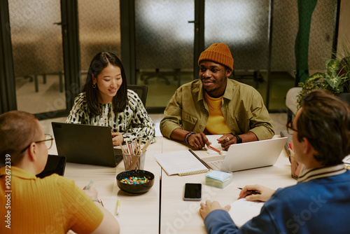 High angle view of multi-ethnic group of young colleagues sitting at table with laptops, gadgets and documents on top, discussing work plan