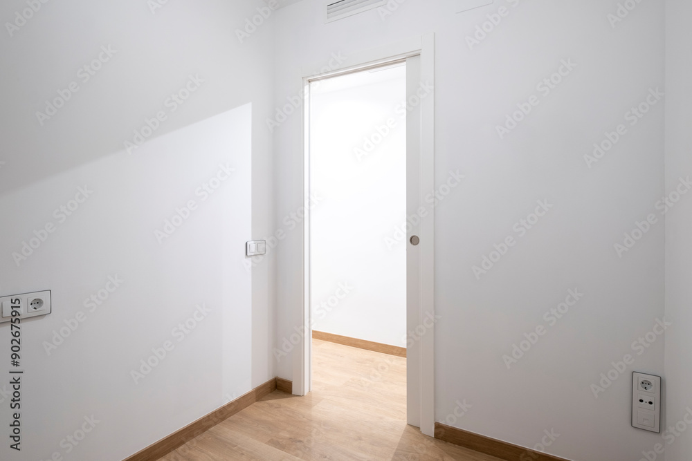 A minimalistic unfurnished white room with clean walls and a smooth wooden floor, featuring an open sliding white door leading to another, well-lit space. A minimalistic unfurnished white room with clean walls and a smooth wooden floor, featuring an open sliding white door leading to another, well-lit space.