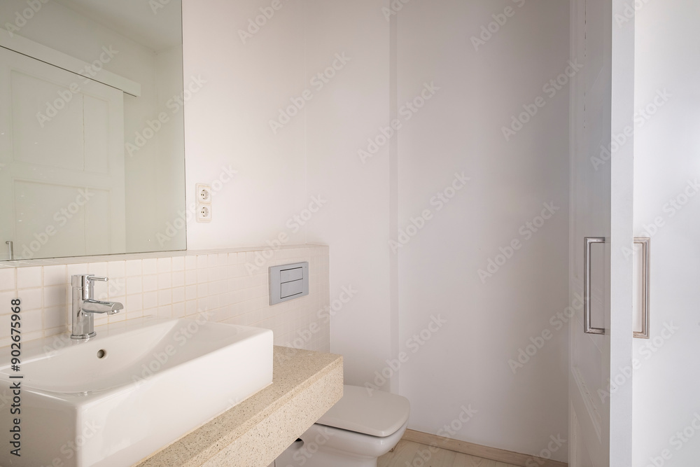 A clean, modern bathroom with white walls, minimalistic design, featuring a sink, countertop, wall-mounted fixtures, and a simple yet modern aesthetic.