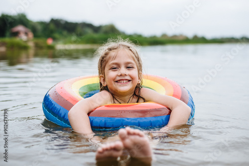 Happy child swims in the river on a colored inflatable circle. Cute little girl gives birth while swimming in the lake. Summer vacation.