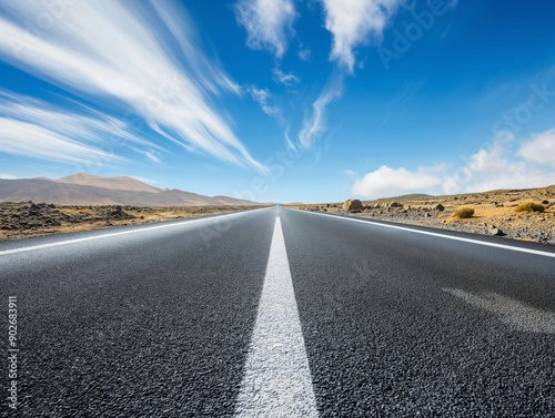 A perspective view of a long road stretching into the distance, leading towards majestic mountains under a bright blue sky, symbolizing adventure and exploration.