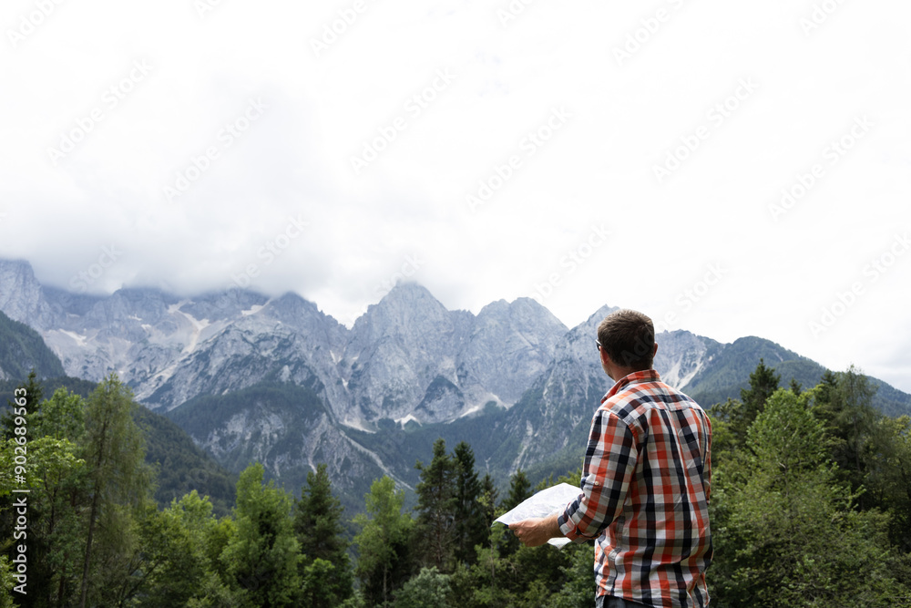 a satisfied man in a checkered shirt holds a map of the area in his hands and looks into the distance at the high mountains on a sunny day a satisfied man in a checkered shirt holds a map of the area in his hands and looks into the distance at the high mountains on a sunny day
