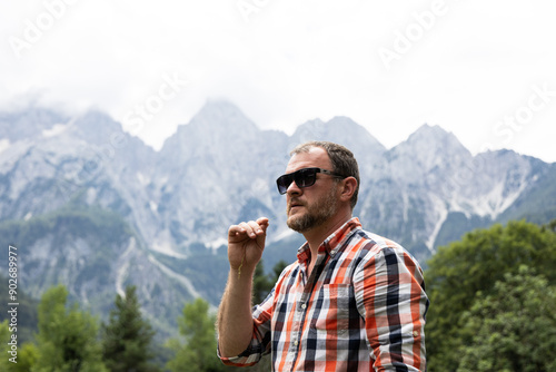 male tourist in a plaid shirt and sunglasses standing against the backdrop of the majestic Mount Triglav in Slovenia. He looks into the distance, enjoying the view of the picturesque mountains, emphas photo