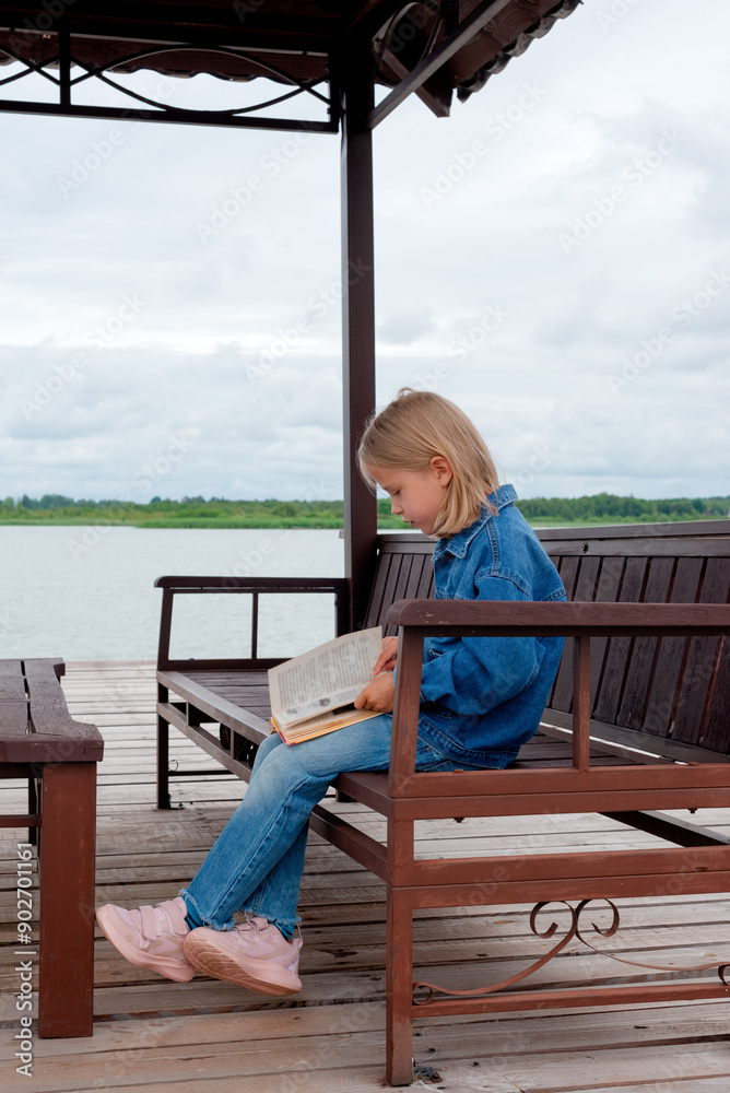 Girl reads a book while sitting in a gazebo on the shore of a lake. Vertical orientation. Girl reads a book while sitting in a gazebo on the shore of a lake. Vertical orientation.