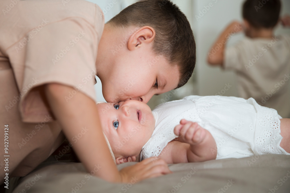 child brothers kisses new born baby which lies on the bed at home. happy siblings. child brothers kisses new born baby which lies on the bed at home. happy siblings.