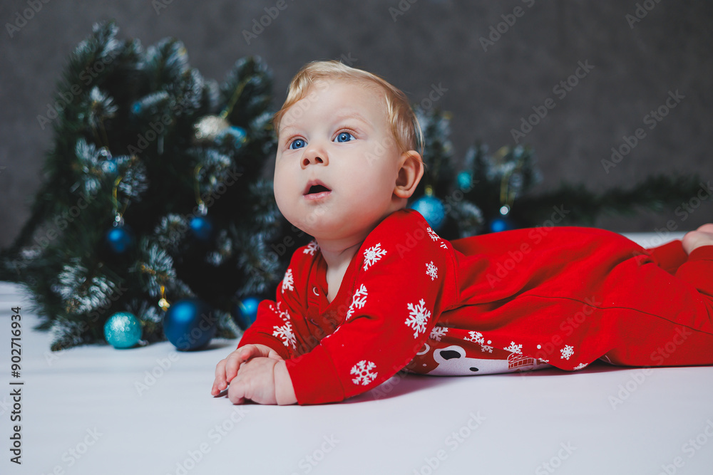 A cute baby in a bodysuit lies near a Christmas tree and gift boxes. New Year's clothes for babies. winter new year concept.