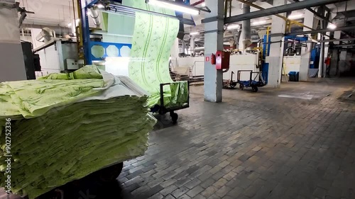  On weaving factory. Stacks of green woven fabric on background of working machine. Intricate process of textile production 