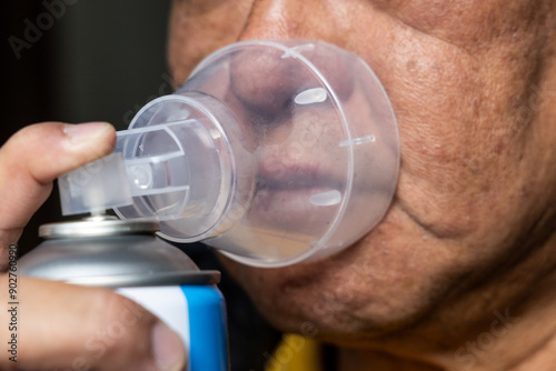 Closeup of elderly Asian man inhaling oxygen from cannister in high altitude mountain area to relieve himself from accute thin air