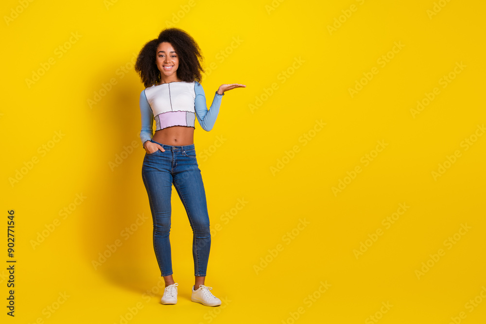Full size photo of pretty young girl hold empty space wear trendy blue outfit isolated on yellow color background Full size photo of pretty young girl hold empty space wear trendy blue outfit isolated on yellow color background