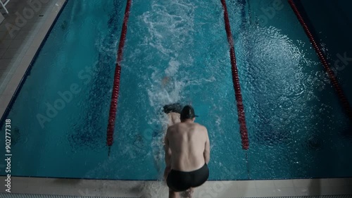 High angle slowmo shot of two professional male swimmers having relay race in indoor pool with lanes