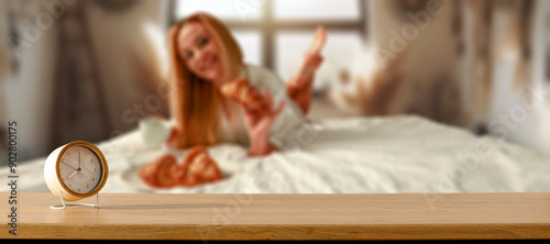 An alarm clock on wooden countertop with copy space. Blurred cozy atmosperic and nostalgic bedroom background with a young woman having breakfast in bed. photo