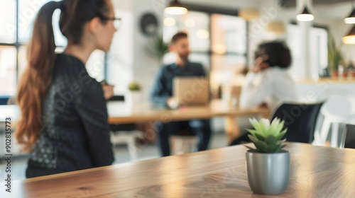 Modern office space with diverse team collaborating: woman in foreground, two colleagues at table. Blurred background highlights professional atmosphere.