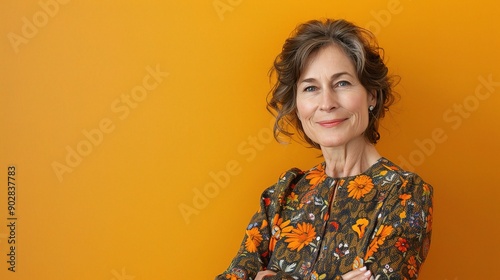 Confident at Any Age: A mature woman with a warm smile and crossed arms exudes confidence against a vibrant orange backdrop.