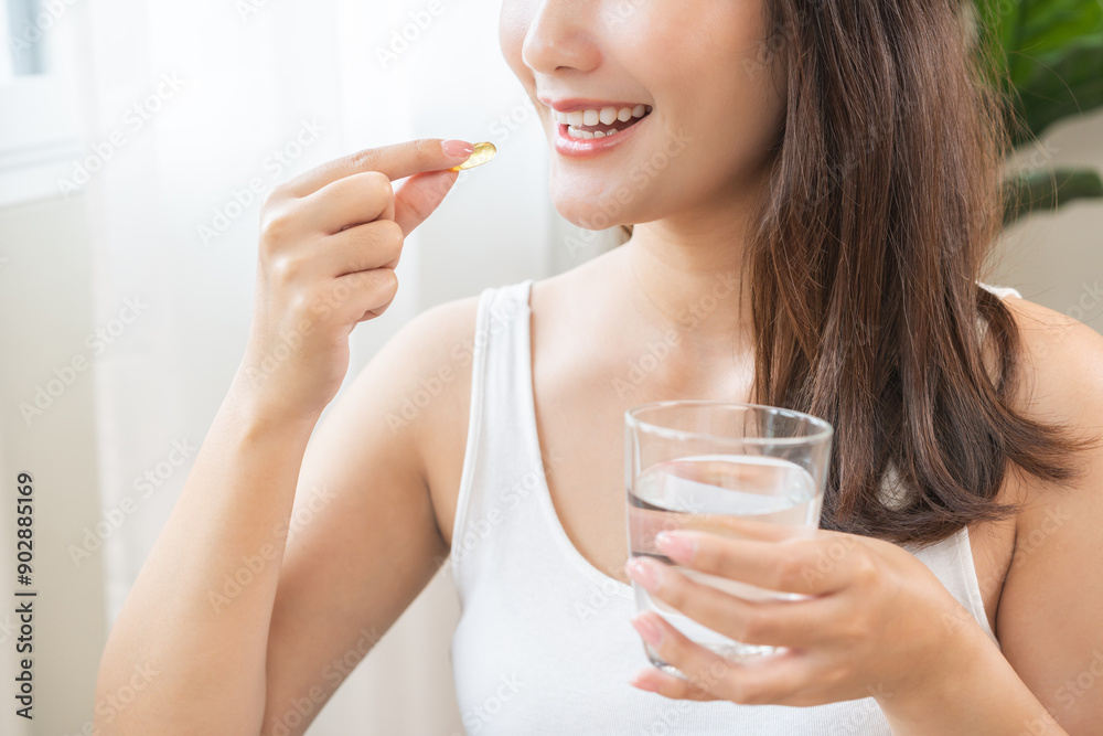 Dietary supplement, asian young woman, girl hand holding fish oil pills, drugs medical, take or eat vitamin for treatment skin, hair and nail strengthen with glass of water at home. Healthcare concept Dietary supplement, asian young woman, girl hand holding fish oil pills, drugs medical, take or eat vitamin for treatment skin, hair and nail strengthen with glass of water at home. Healthcare concept
