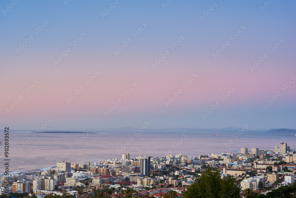 Naklejka premium Cityscape, sunset and water or urban landscape with buildings, tree and sea or outdoor. Development, skyline and coastline for shipping, cargo and tourism or travel for architecture and hospitality