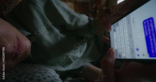 A woman uses a mobile phone lying in bed at home. Close-up of her hands, an unrecognizable person