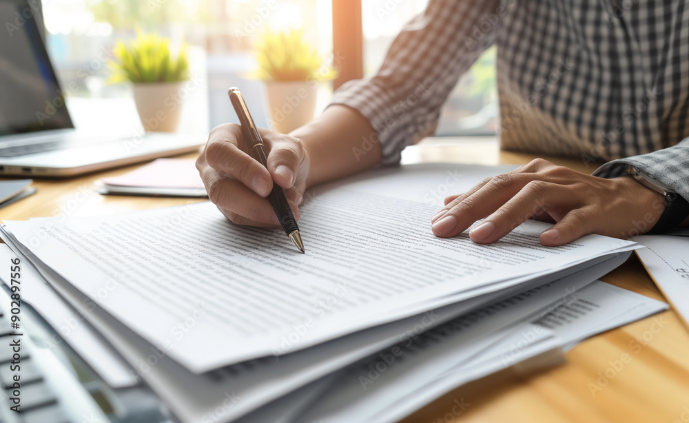 Person writing on papers with a pencil at a desk.