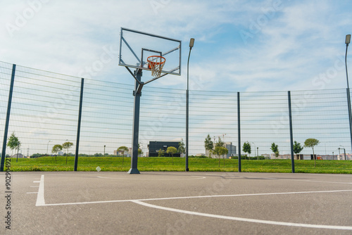 Outdoor basketball court with a metal hoop and fencing, captured under a vibrant, clear blue sky. photo