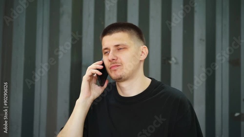 A man with a short haircut speaks. teleon on the street.
Gray background.
Phone conversation.
Guy with a phone in his hands photo