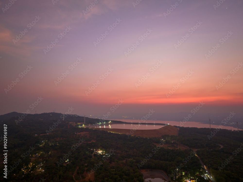 Fototapeta premium A serene aerial view of a reservoir reflecting the warm colors of the sunset. wind turbines in the distance. The scene captures the tranquility of nature and the harmony of renewable energy.