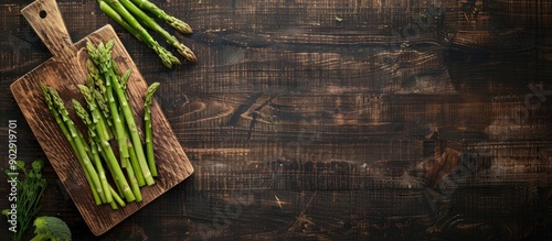 Top down copy space image presents fresh asparagus steams on a cutting board over a dark wooden background ready for cooking