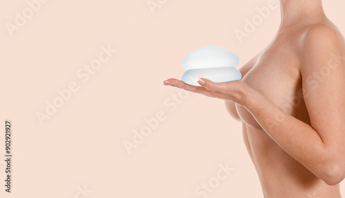Woman holding implants on hand on beige background. Breast augmentation