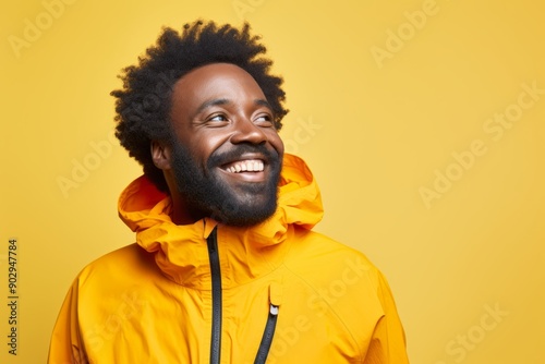 Portrait of a glad afro-american man in his 40s wearing a windproof softshell in front of pastel yellow background