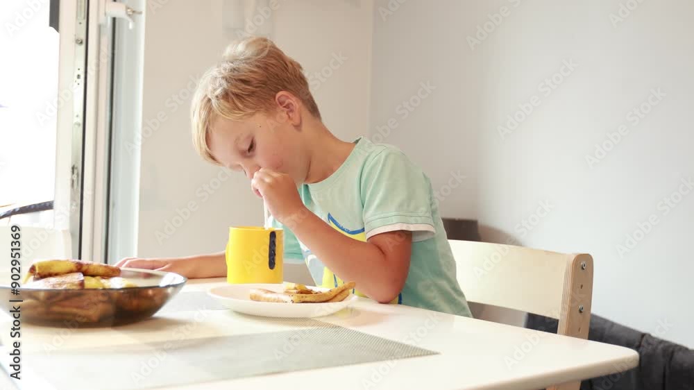 Caucasian Boy Enjoys Breakfast at His Kitchen Table While Sipping From a Yellow Cup Caucasian Boy Enjoys Breakfast at His Kitchen Table While Sipping From a Yellow Cup
