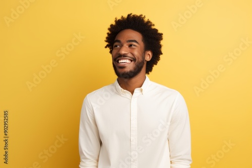 Portrait of a happy afro-american man in his 20s wearing a classic white shirt over pastel yellow background