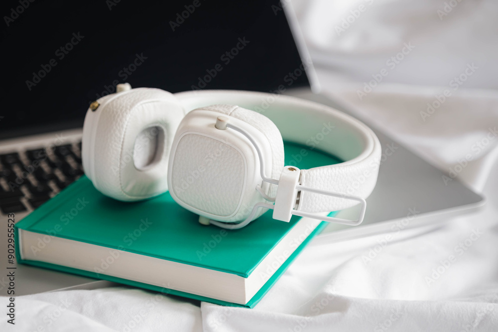 White headphones, book and laptop in a white bed, hobby, work at home, lazy day off. White headphones, book and laptop in a white bed, hobby, work at home, lazy day off.