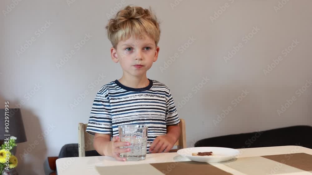Curious Caucasian Boy Enjoys Snack While Sitting at Kitchen Table During Daytime Curious Caucasian Boy Enjoys Snack While Sitting at Kitchen Table During Daytime