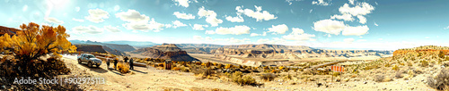 A car parked at a highway overlook, with people taking photos and enjoying the view
