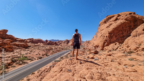 Man standing on endless winding empty Mouse tank road in Valley of Fire State Park through canyons of red Aztec Sandstone Rock formations and desert vegetation in Mojave desert, Overton, Nevada, USA