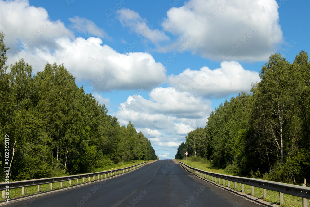 A Beautiful Scenic Open Road Stretching Under a Bright Blue Sky with Fluffy White Clouds A Beautiful Scenic Open Road Stretching Under a Bright Blue Sky with Fluffy White Clouds