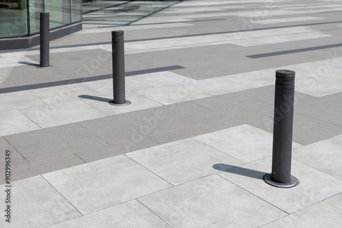 Three black poles are standing in a row on a gray and white sidewalk photo