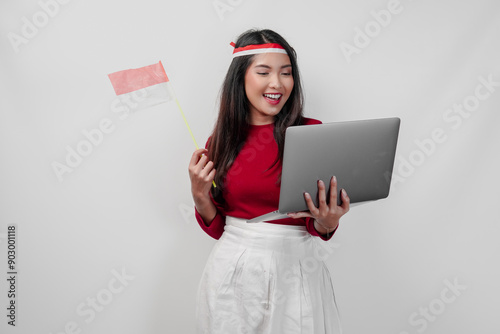 Joyful young Asian woman is holding a laptop and a mini country flag. photo