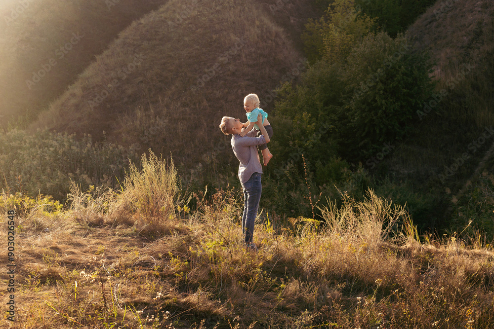 Mother and her little son enjoy they time in nature in summer with sun rays on sunset near green hills Mother and her little son enjoy they time in nature in summer with sun rays on sunset near green hills