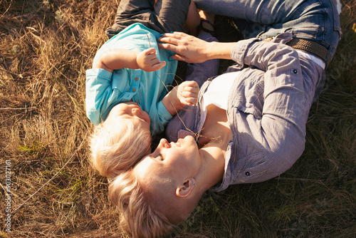 Mother and her little son and liying on the grass and hugging in summer with sun rays on sunset photo