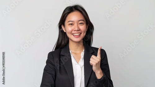 Happy young Asian business woman in blazer pointing finger up isolated on white background