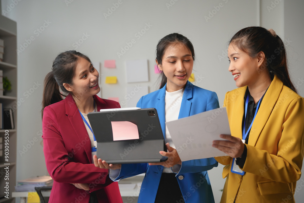 Three young businesswomen are collaborating on a project, using a tablet and documents to review data and strategize their next steps Three young businesswomen are collaborating on a project, using a tablet and documents to review data and strategize their next steps