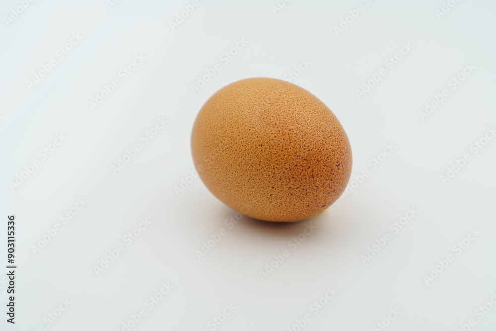A lone brown egg is positioned on a clean white surface. The shell displays tiny blemishes and a feather, suggesting its organic farm origin. Ideal for preparing nutritious meals and recipes. A lone brown egg is positioned on a clean white surface. The shell displays tiny blemishes and a feather, suggesting its organic farm origin. Ideal for preparing nutritious meals and recipes.