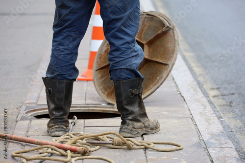Worker standing over the open sewer hatch on city street. Concept of repair of sewage, underground utilities, water supply system, cable laying, water pipe accident