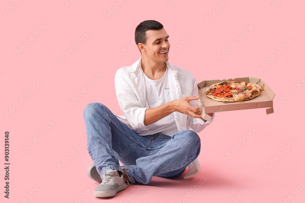 Young man with tasty pizza sitting on pink background Young man with tasty pizza sitting on pink background