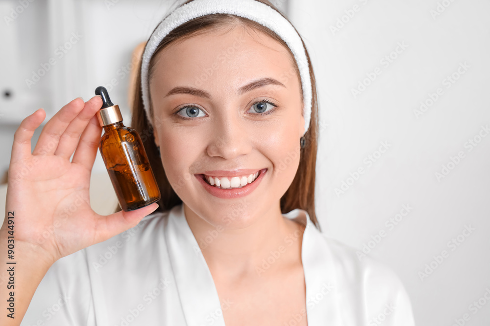 Fototapeta premium Smiling young woman holding amber dropper bottle with skincare serum, beauty routine and facial treatment