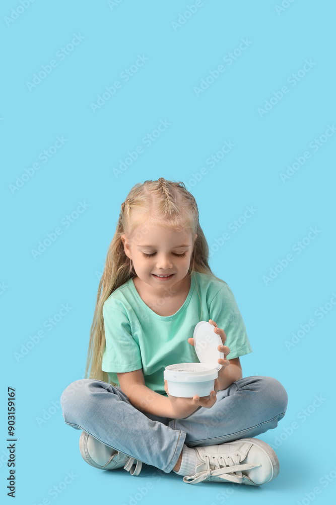 Cute little girl with tooth powder sitting on blue background Cute little girl with tooth powder sitting on blue background